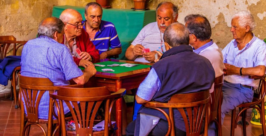 A group of older men, all close friends sitting around a table playing cards.